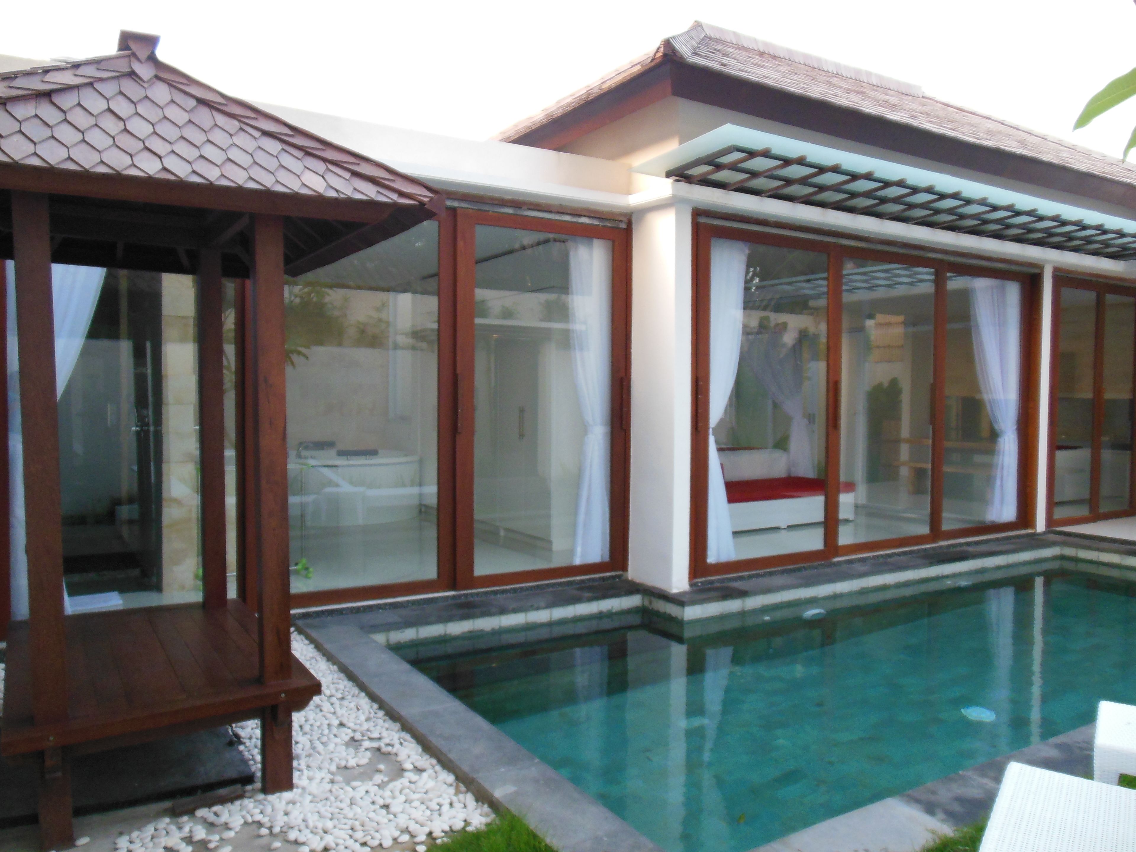 Piscina com deck de madeira e sala envidraçada com um banco estofado vermelho.