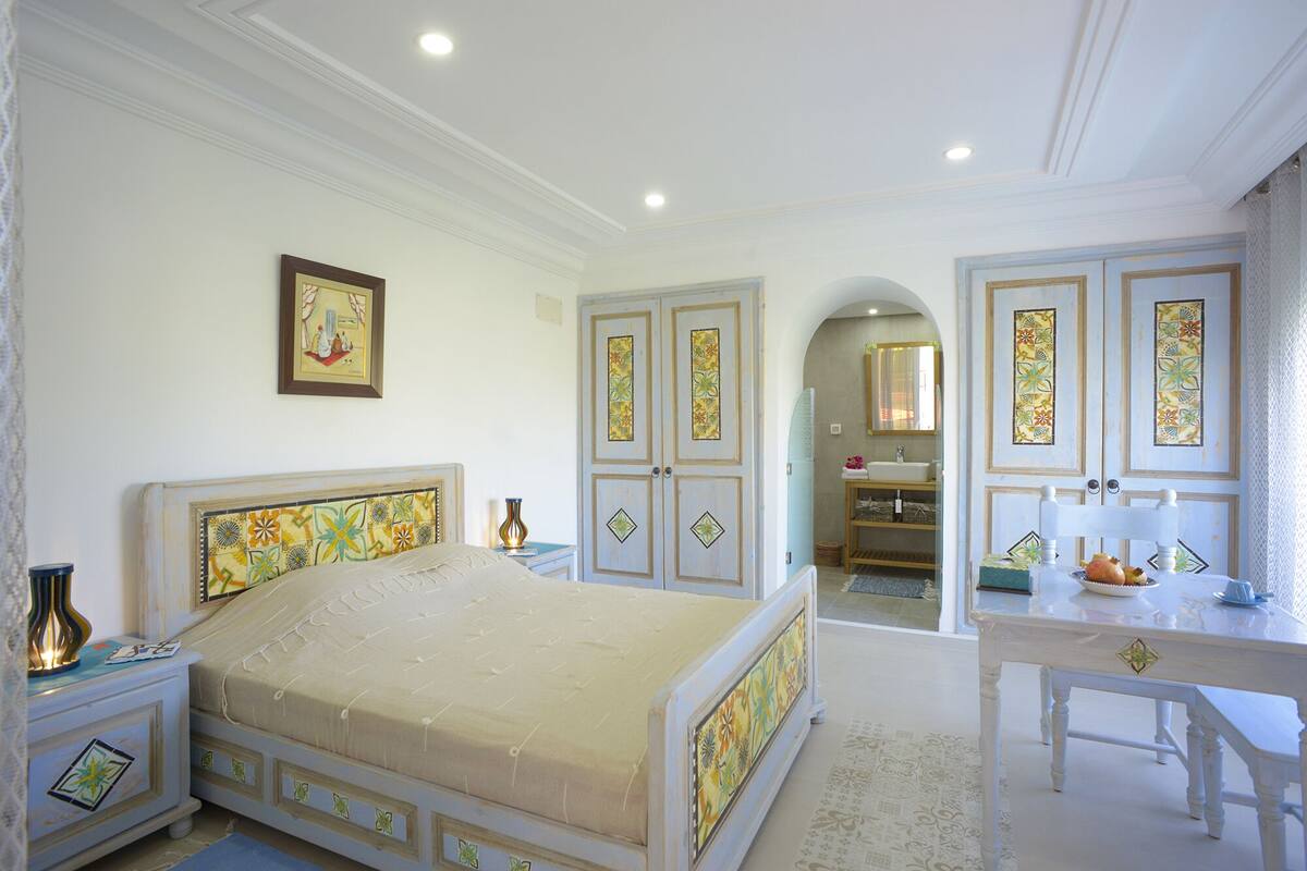 A bedroom with a bed, a bedside table, a dresser, and a mirror.