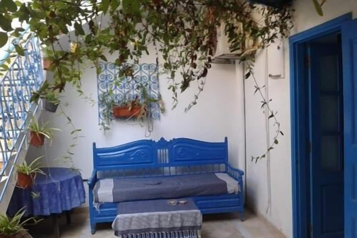 A small, enclosed room with a blue bed, a small table, and potted plants.