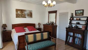 Un dormitorio con una cama de madera, un banco, un aparador con libros, un espejo y una araña.