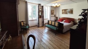 A room with a wooden floor, a bed with a red and white bedspread, a wooden chair, a wooden desk, and a chandelier.