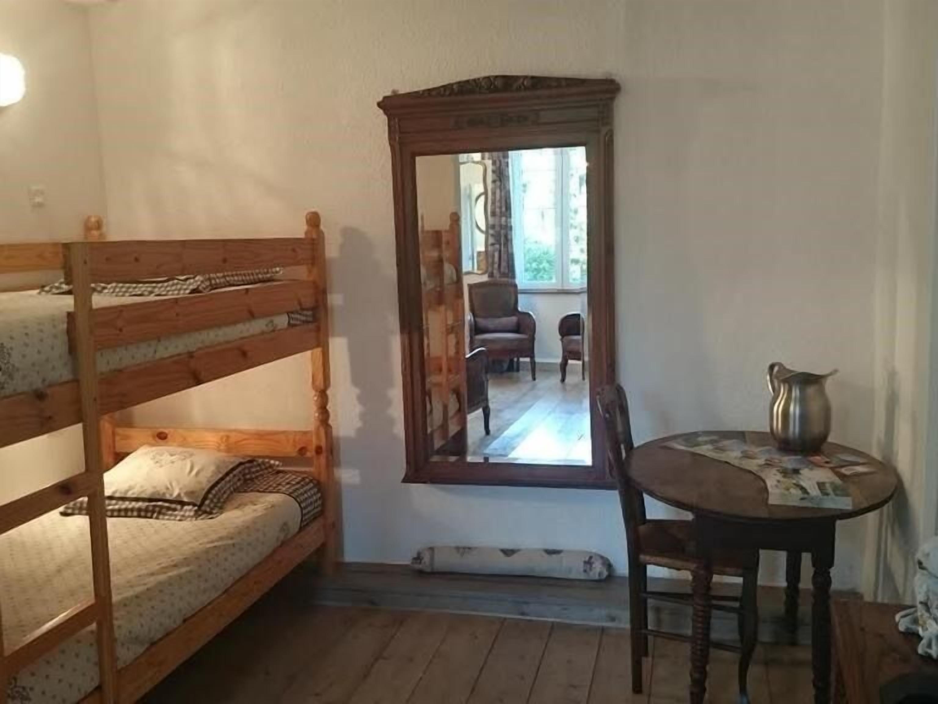 A small room with a bunk bed, a mirror, a table with a pitcher, and a chair.