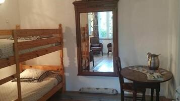 A small room with a bunk bed, a mirror, a table with a pitcher, and a chair.
