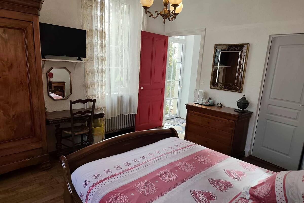 Une chambre à coucher comprenant un lit, une commode, un miroir, un téléviseur et une porte donnant sur une autre pièce.