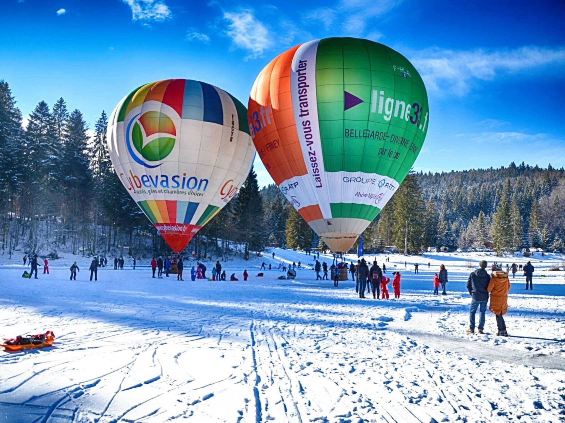 Dos globos aerostáticos sobre un paisaje nevado, con gente cerca.