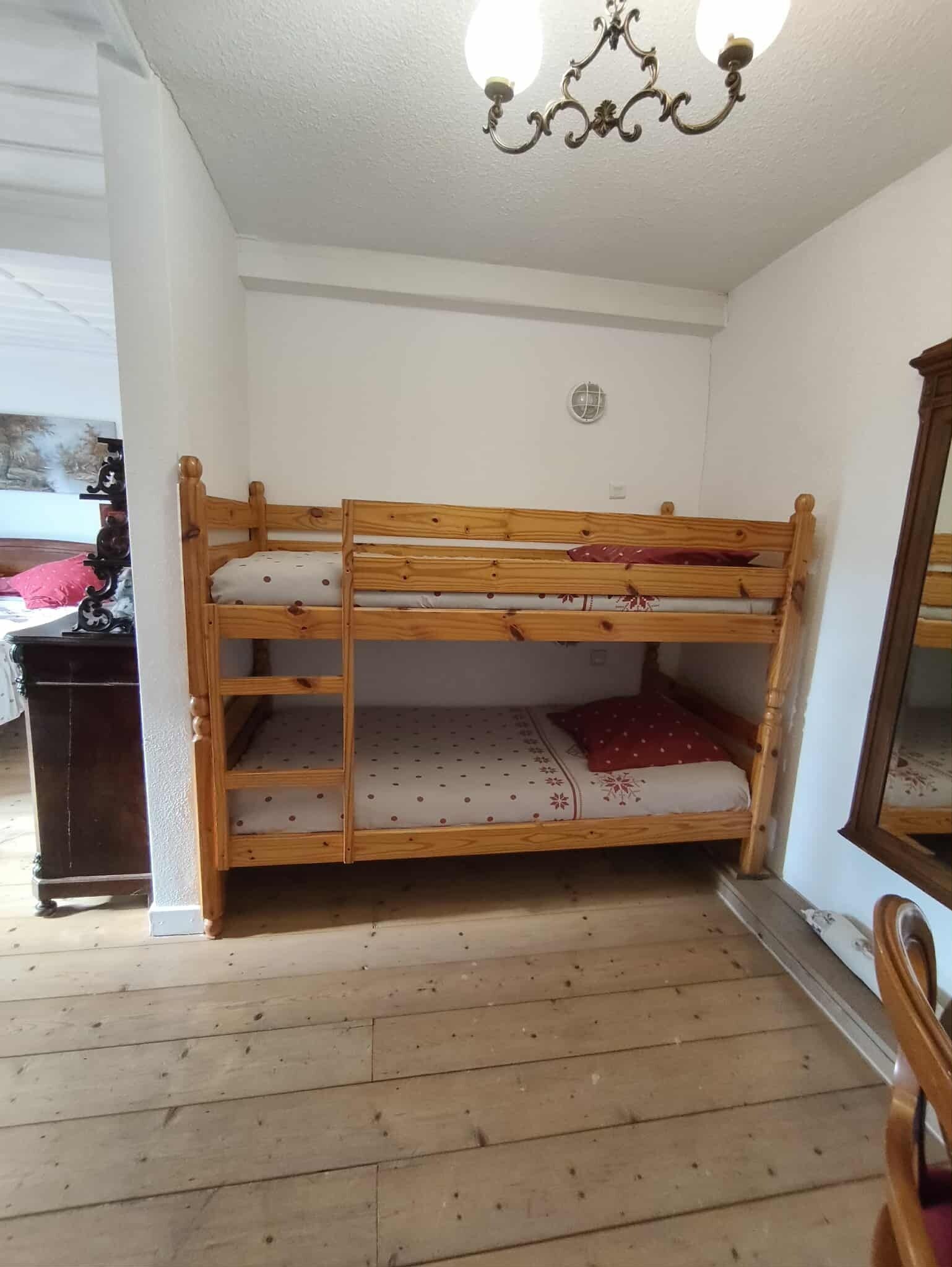 A bunk bed in a room with white walls, a wooden floor, and a chandelier.
