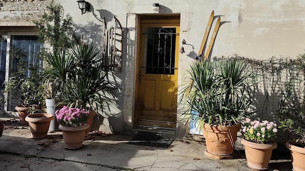 A building with a yellow door, potted plants, and a metal balcony railing.