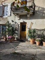 Un edificio con puerta amarilla, plantas en macetas y barandilla de balcón metálica.