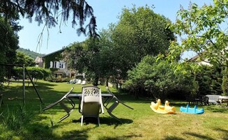 Un jardín con una mesa y sillas, una hamaca y una zona de juegos con juguetes amarillos y azules.