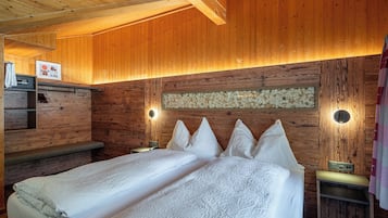 A wooden cabin-style room with two beds, a wooden bench, a small table, and a wall-mounted radio.