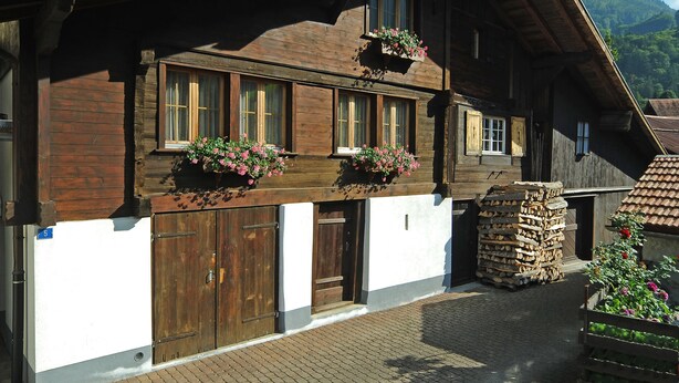 Ein traditionelles Holzhaus mit großen Fenstern, einer Holztür und Blumenkästen an den Fensterbänken.