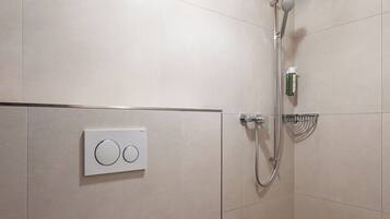 Une salle de bain moderne avec un plafond en bois, des toilettes, une douche avec un pommeau de douche à main et un panneau de commande fixé au mur.
