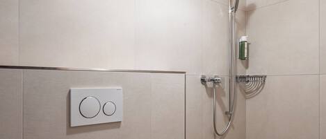 A modern bathroom with a wooden ceiling, a toilet, a shower with a handheld showerhead, and a wall-mounted control panel.