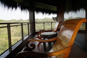 A wooden bench with a round table on a balcony with a view of a forest. - Samboja Lodge (Balikpapan)