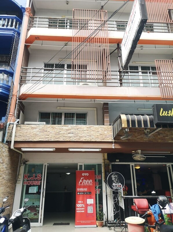 A multi-story building with a ground-level entrance, a balcony with a metal railing, and a sign for 'K.J.S HOUSE'.