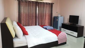 A neatly arranged bedroom with a bed, a television, a small fridge, and a cabinet.