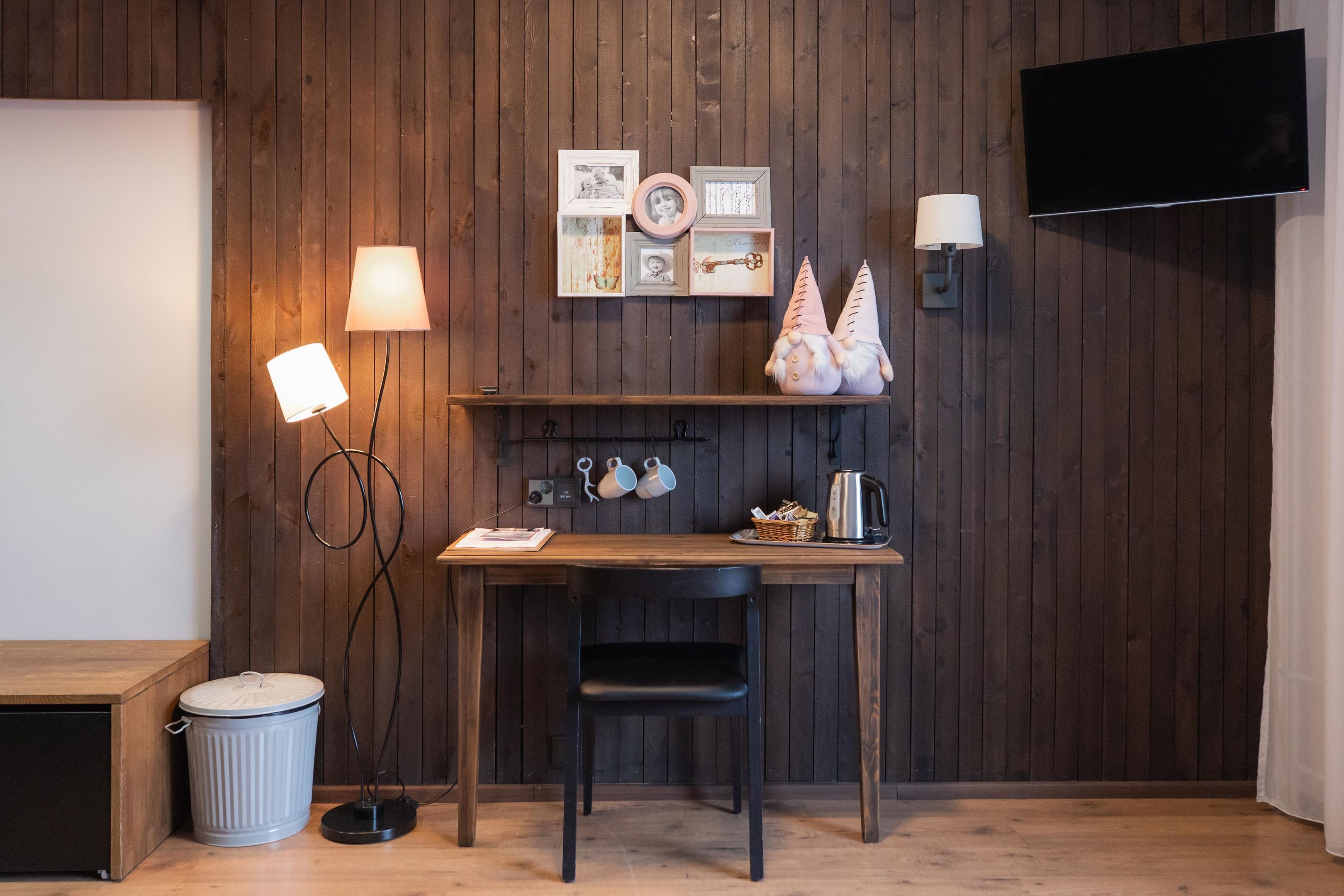 Une pièce aux murs lambrissés, comprenant un bureau, une chaise, deux lampes fixées au mur, un téléviseur et une poubelle.