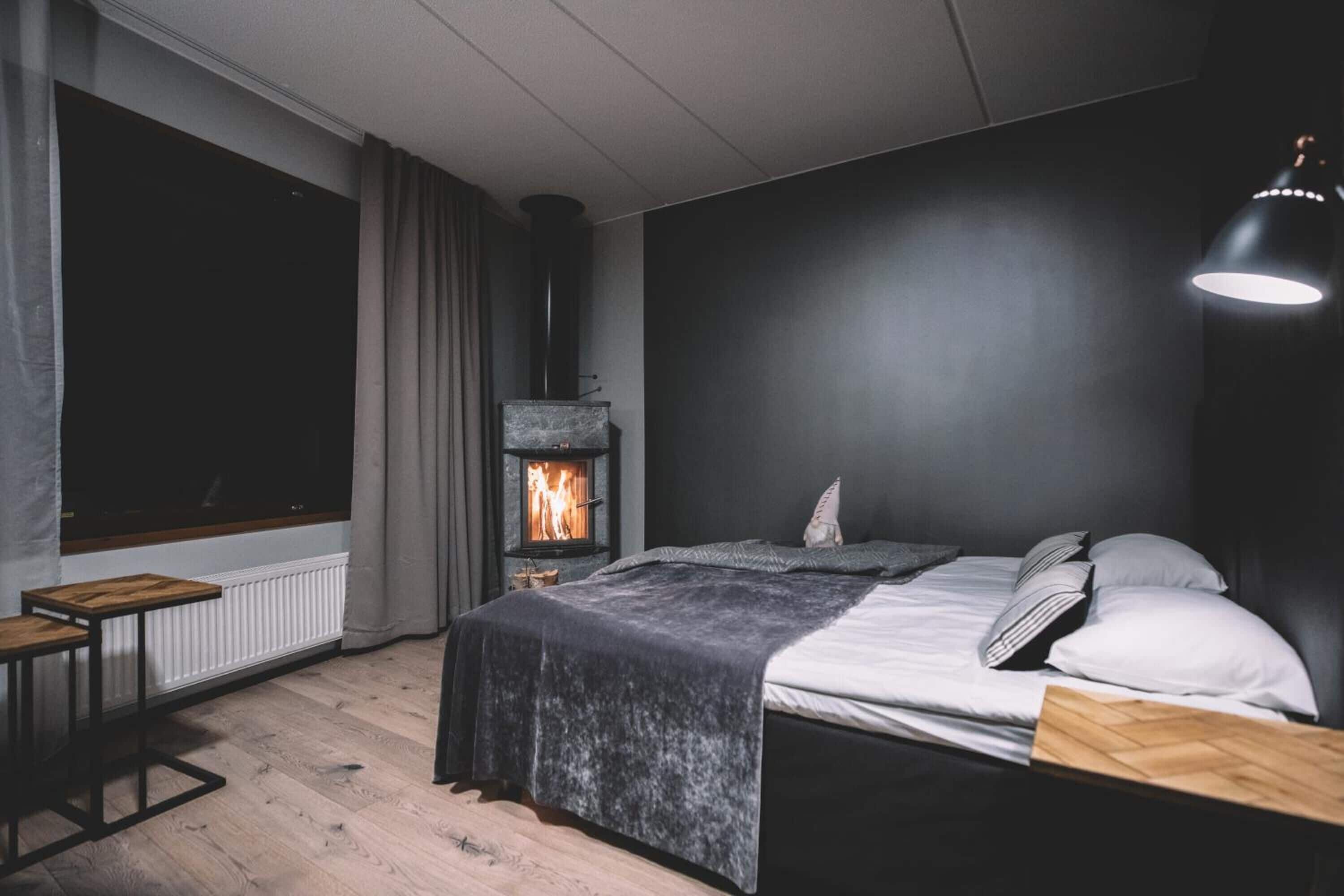 Een moderne slaapkamer met een houtkachel, een bed met wit beddengoed, een nachtkastje en een groot raam.