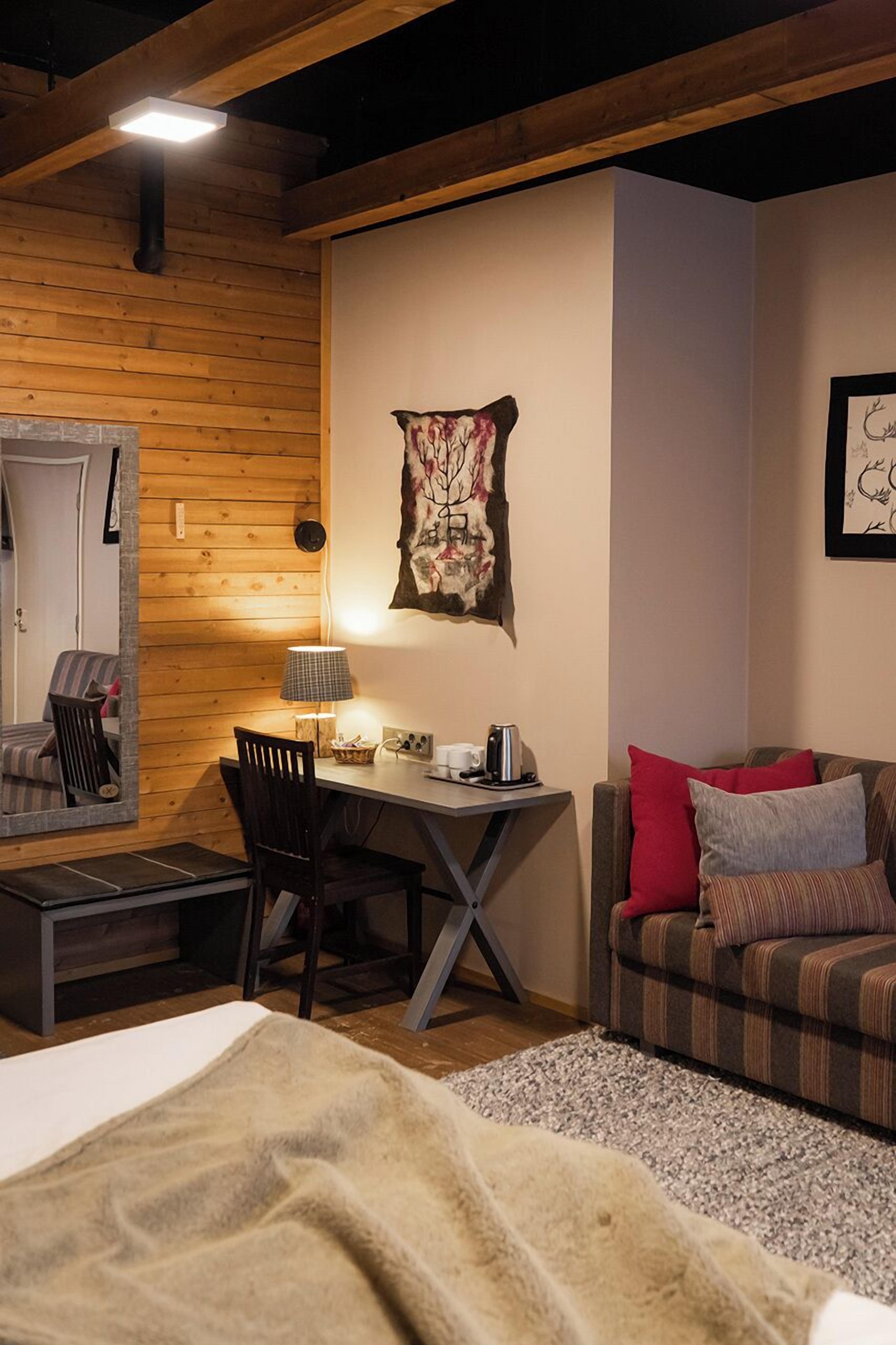 A cozy room with a wooden ceiling, a desk with a lamp, a chair, a couch with pillows, and a large mirror.