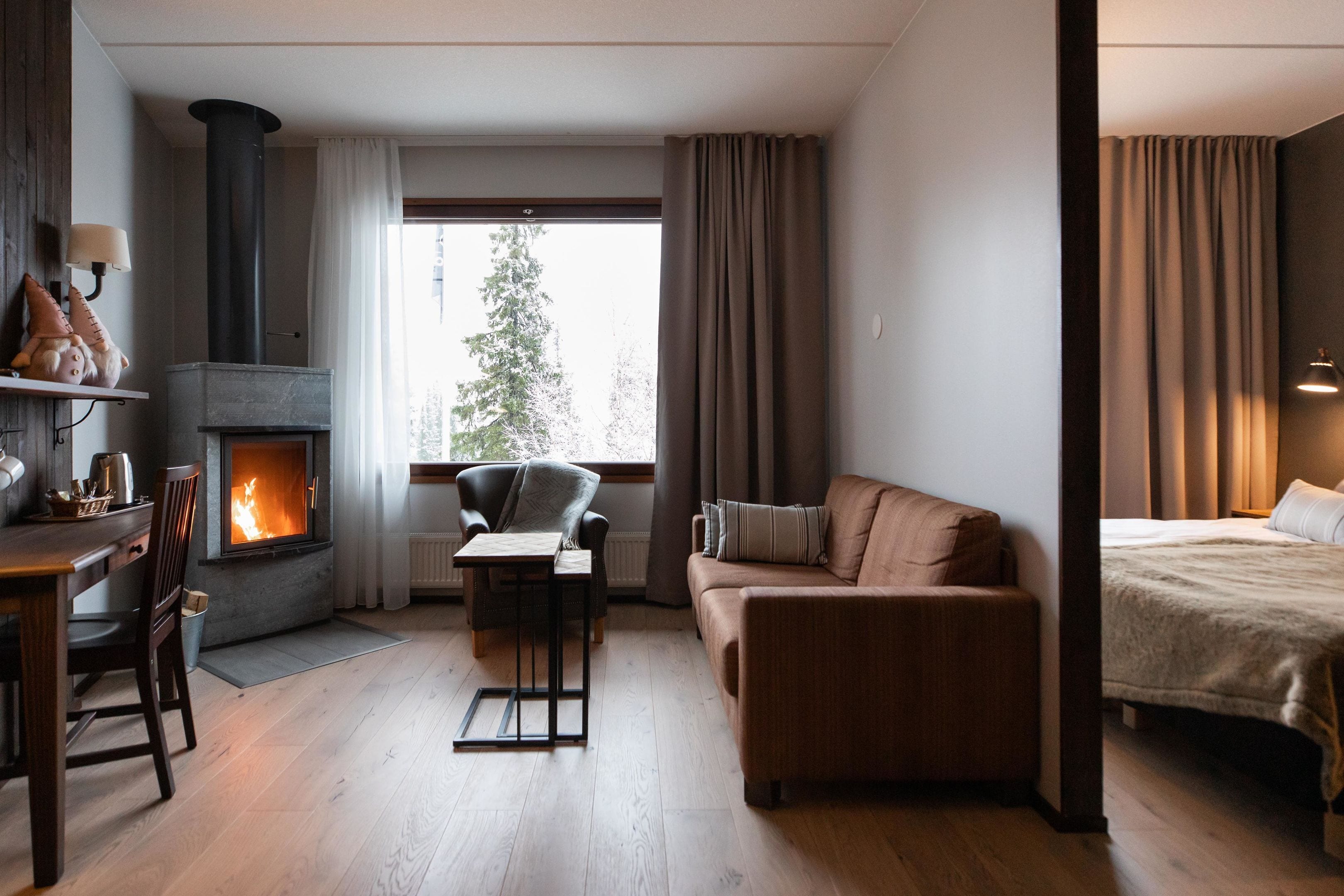 Una sala moderna con chimenea, un sofá, una mesa de comedor y vista a un árbol fuera.
