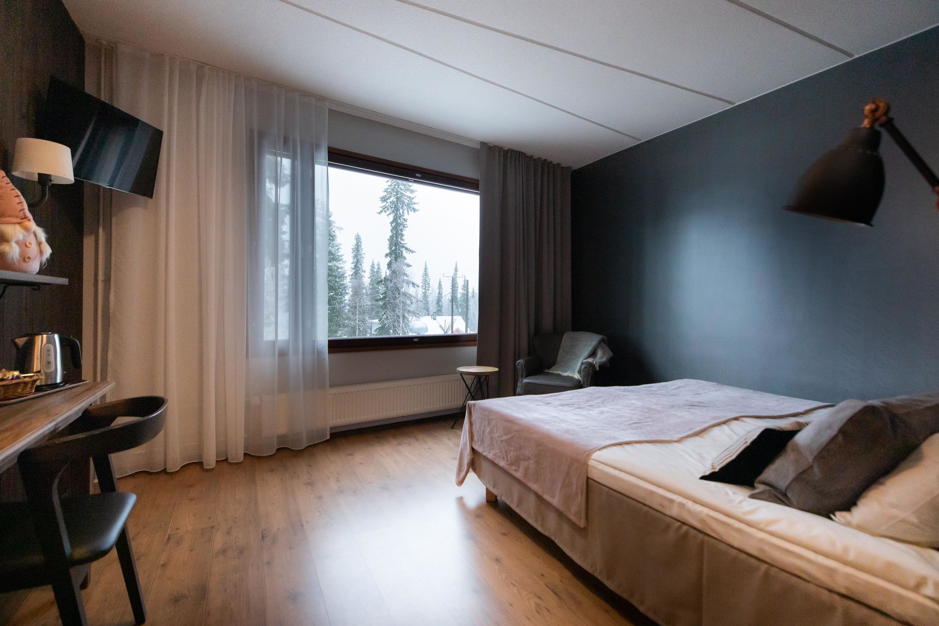A bedroom with a bed, a desk, a chair, a TV, and a window with a view of trees.