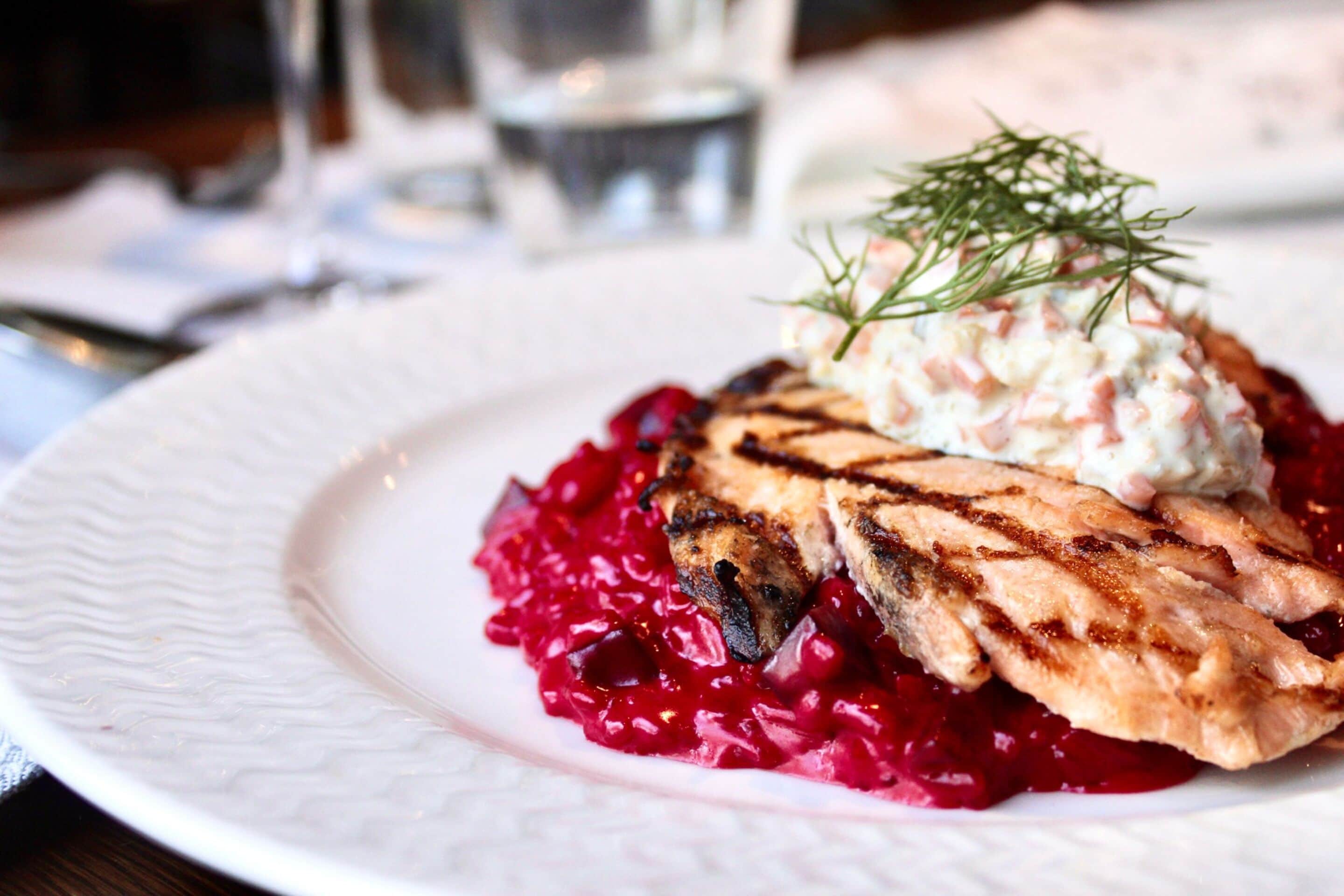 Une assiette contenant du poulet grillé, une cuillerée de sauce crémeuse et quelques brins d’aneth en guise de décoration, le tout servi sur un lit de chou rouge.