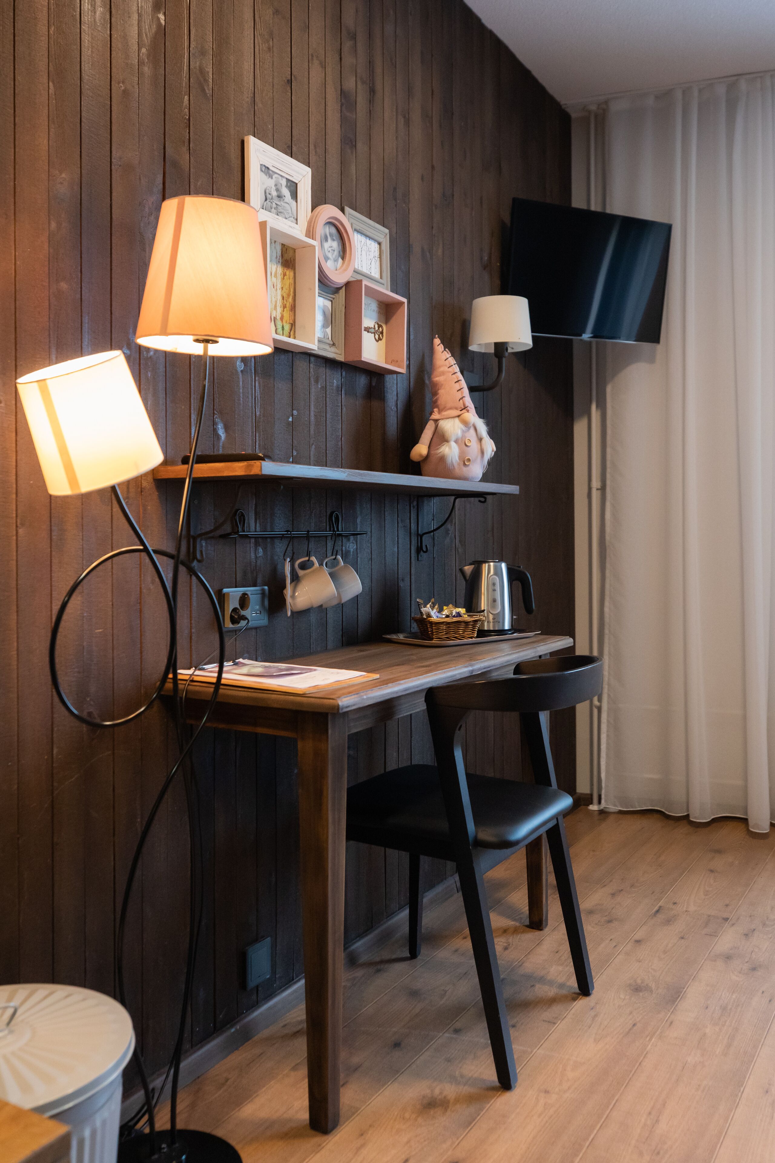 A cozy room with a wooden desk, a lamp, a television, and a shelf with decorative items.