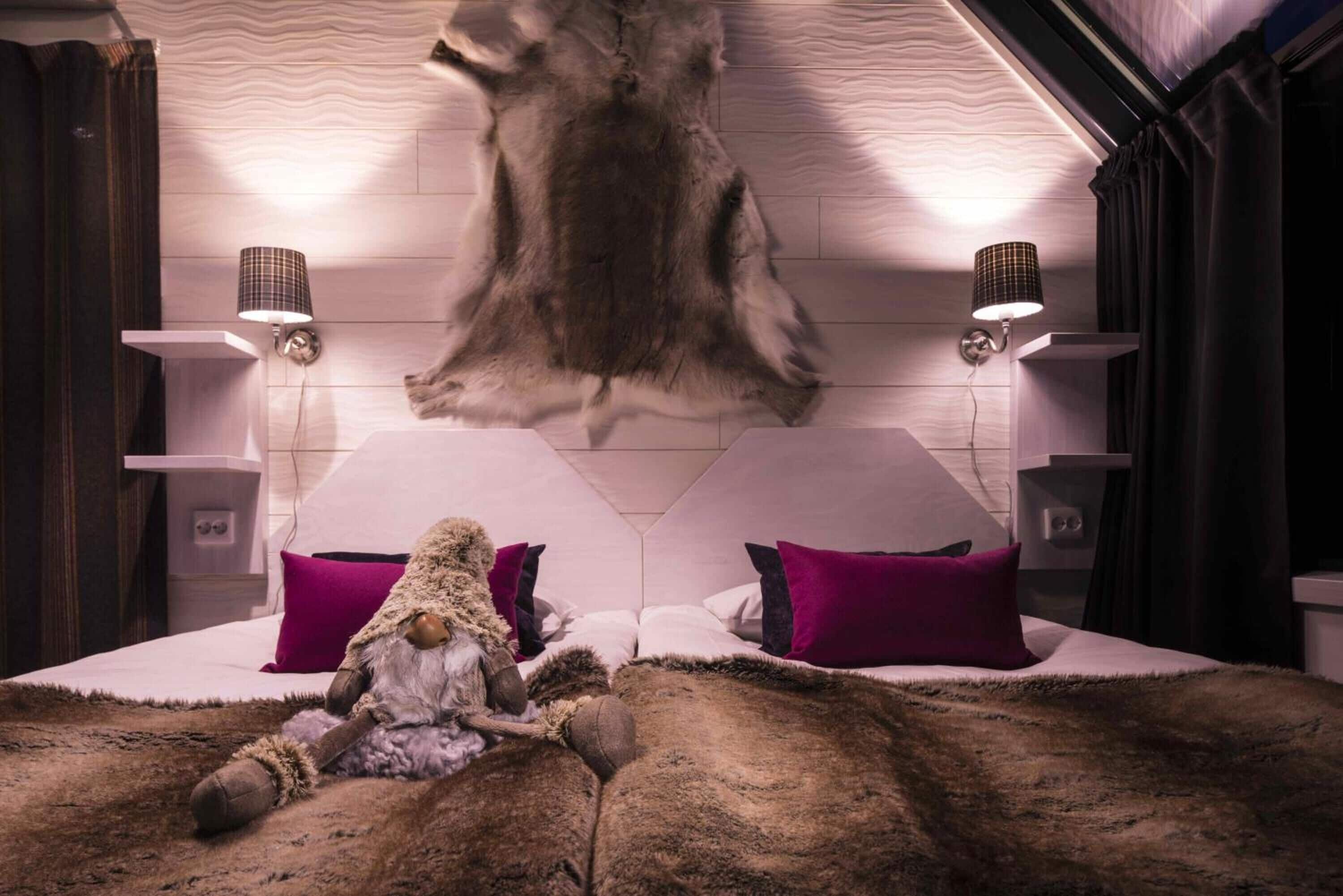 A bedroom with a large fur rug, two purple pillows, a stuffed animal, and a mounted fur headpiece on the wall.
