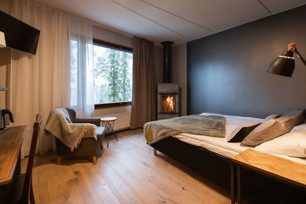 Un dormitorio moderno con cama, una silla, una mesa, chimenea y televisor.