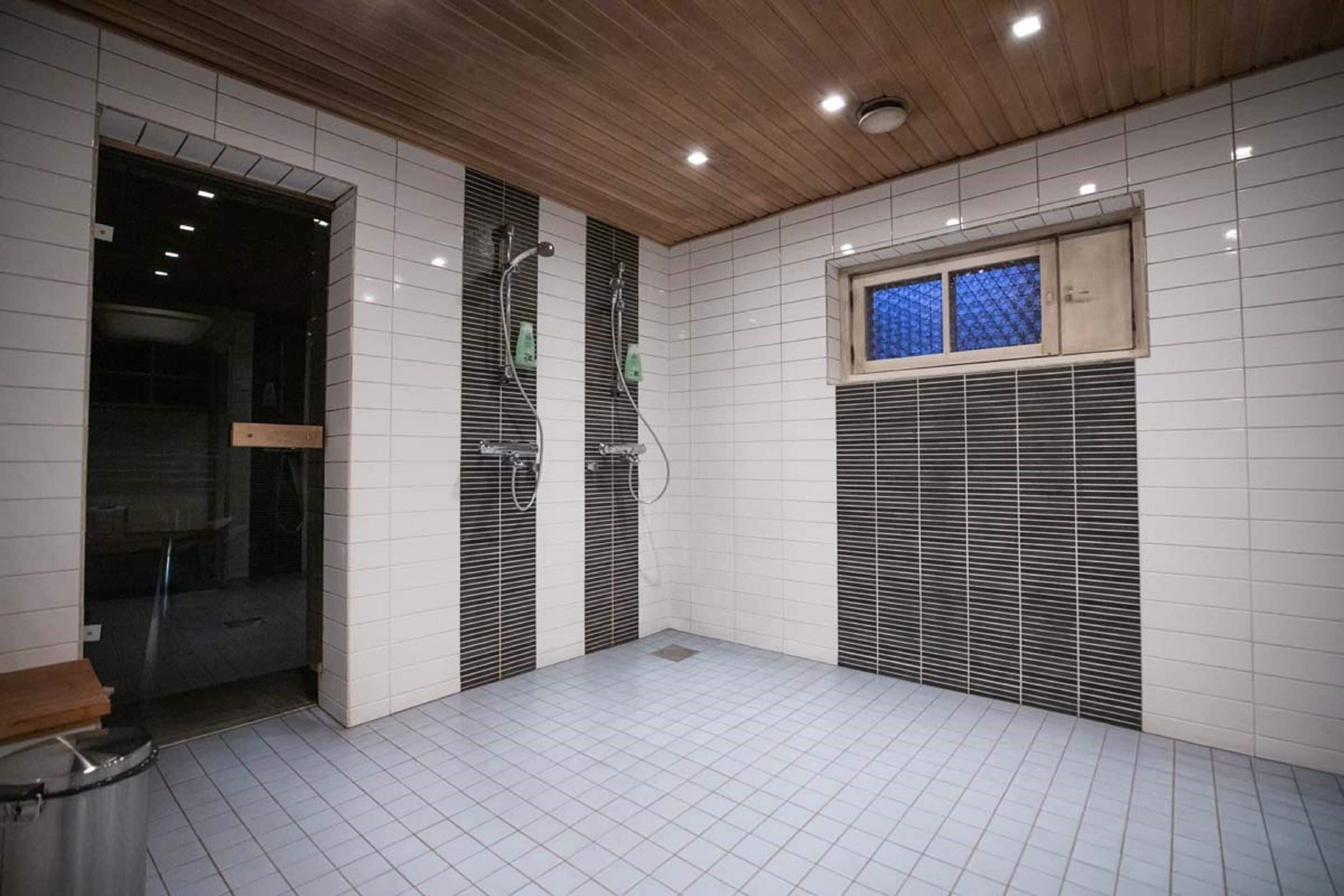 A bathroom with white tiled walls, a wooden ceiling, and a window with blue-tinted glass.