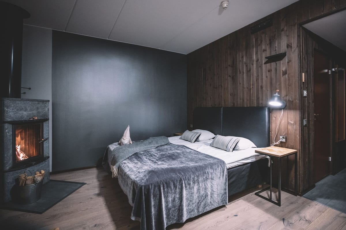 Un dormitorio con una cama, una mesita de noche, un muro de madera y una chimenea.