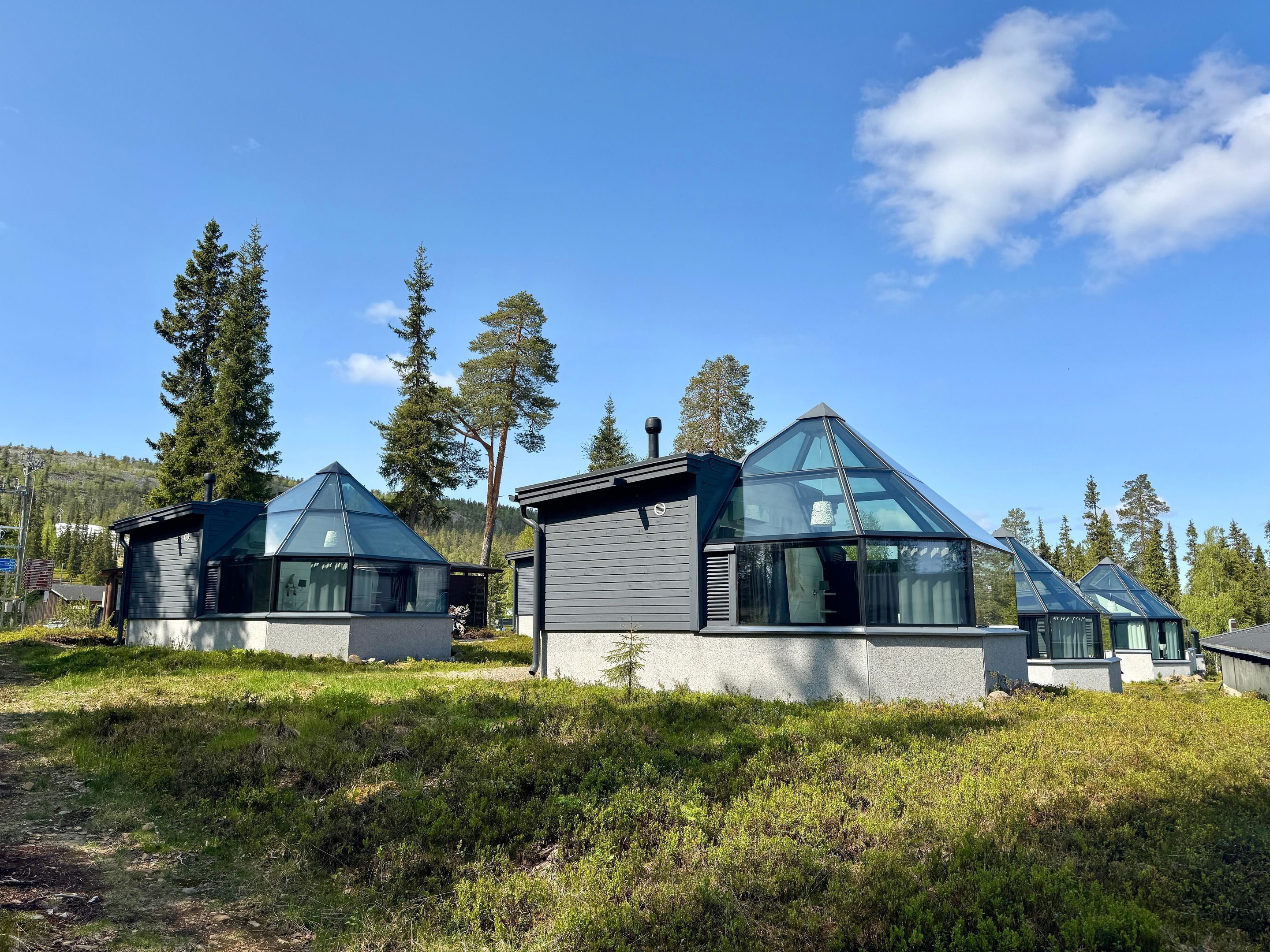 Un edificio moderno de estilo cabaña con techo triangular, rodeado de un paisaje natural con árboles y cielo despejado.