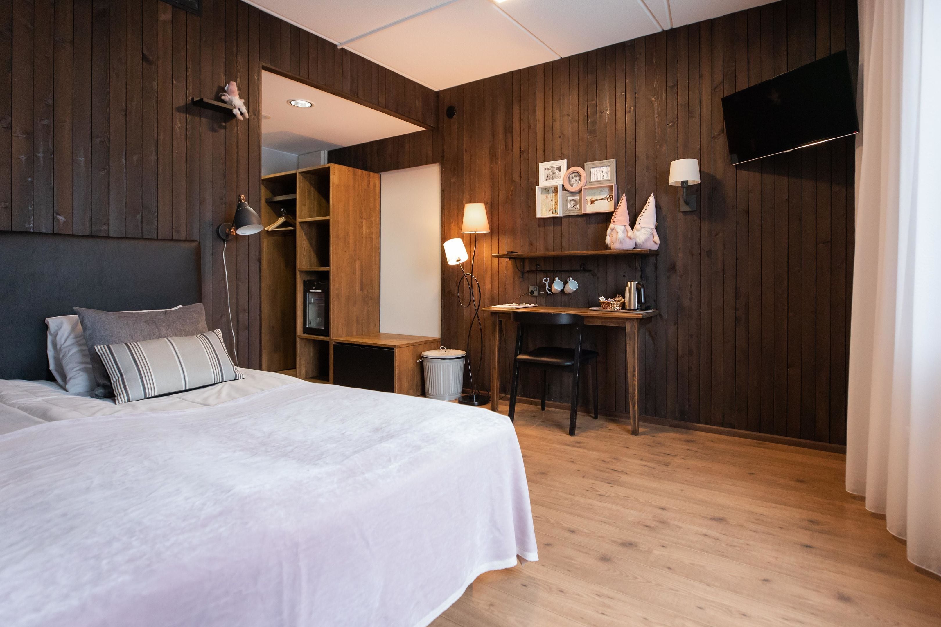 Et soveværelse med seng, sengebord, lampe og et skrivebord med stol.
