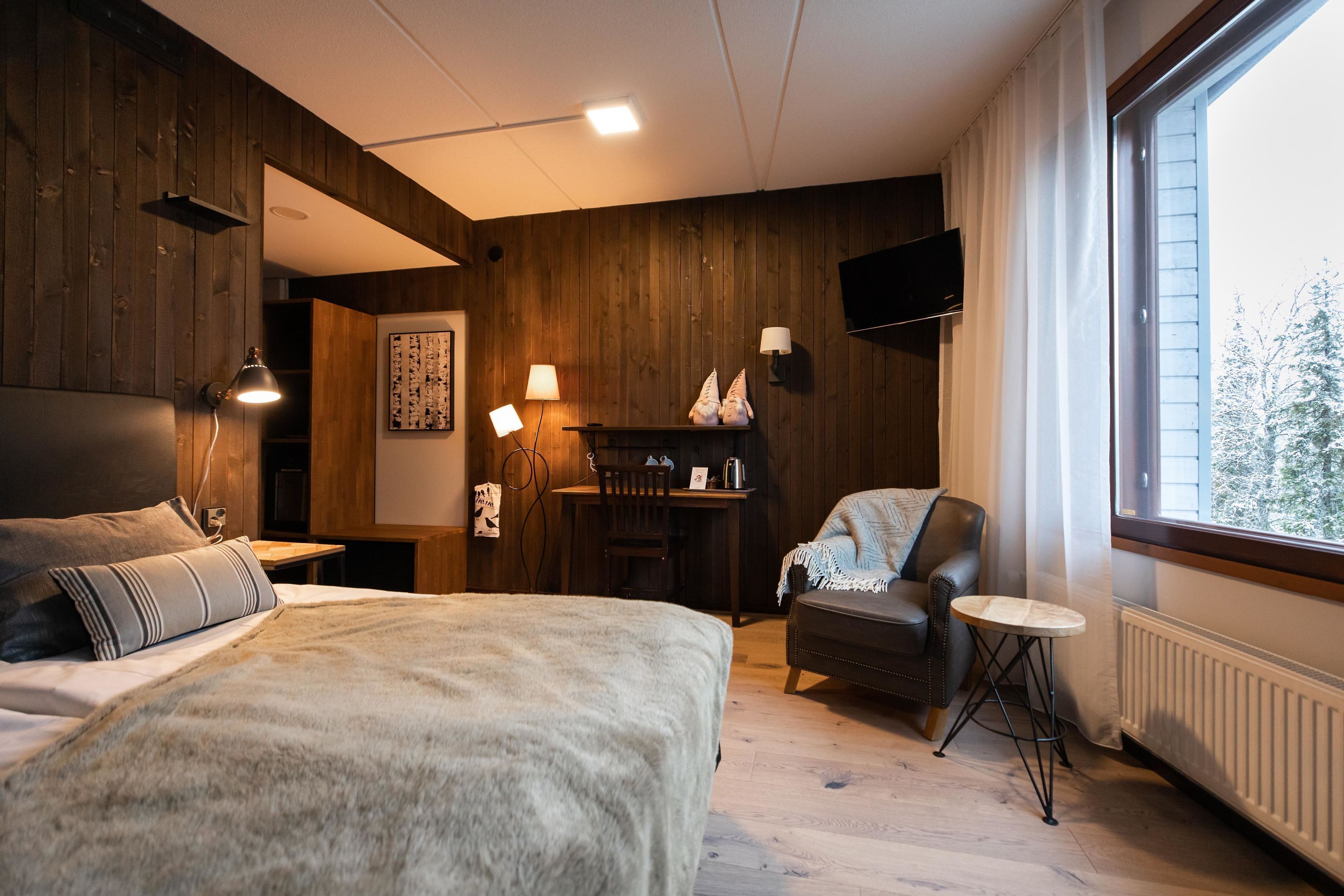 Un dormitorio con una cama, una silla, una mesita, un escritorio y un televisor montado en la pared.