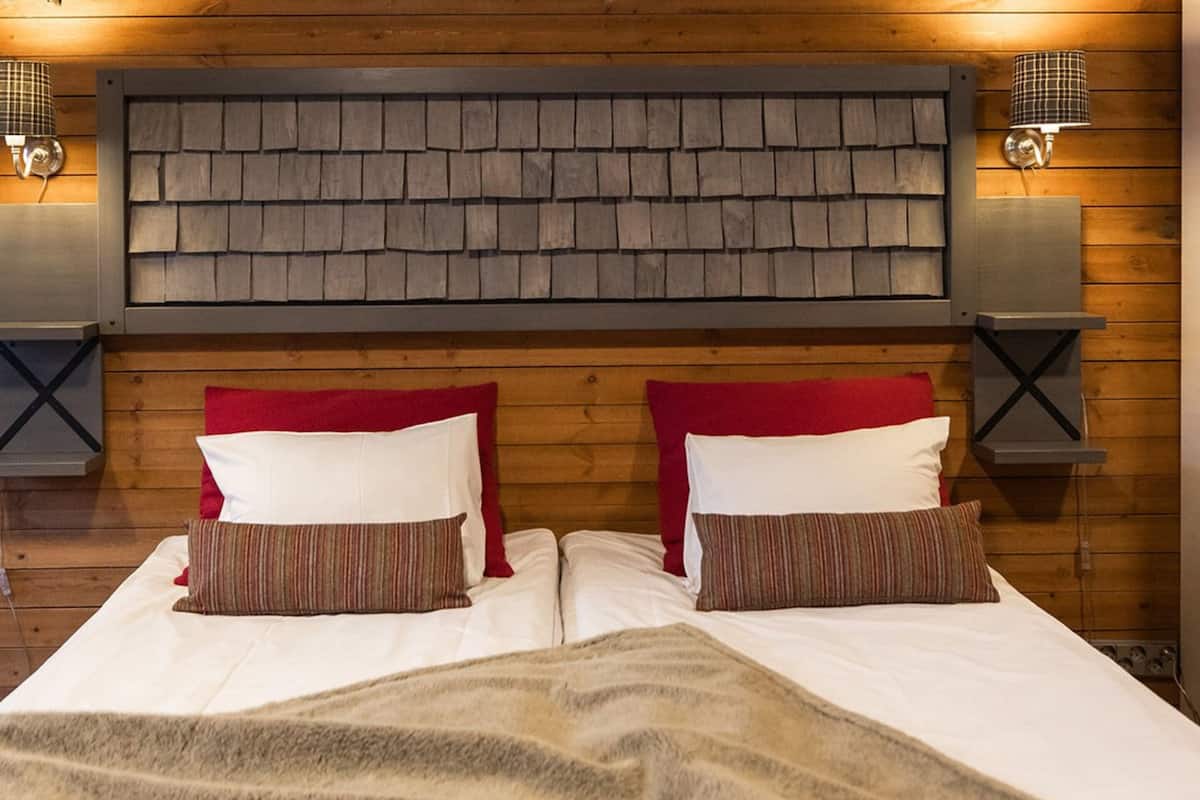 Una cama doble con dos almohadas, cabecera con diseño texturizado y dos lámparas fijadas a la pared.