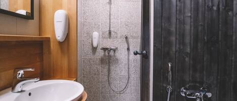 A bathroom with a wooden vanity, a sink, a mirror, a shower with a handheld showerhead, and a dark wooden door.