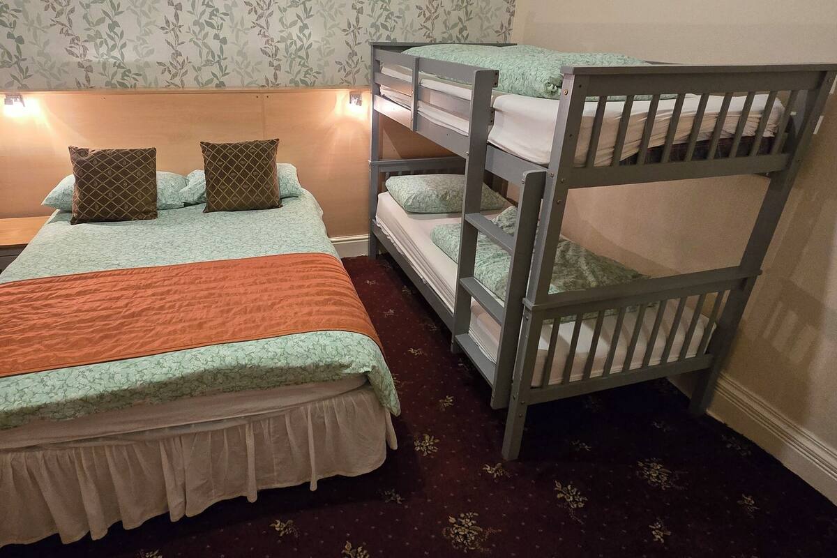 A room with a bunk bed, a desk with a chair, and a bed with a patterned bedspread.
