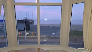 A room with a large window offering a view of the beach, a table, and a fan. - The Sands Hotel (Blackpool)