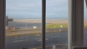 A view from a window overlooking a road with a grassy area and a body of water in the distance. - The Sands Hotel (Blackpool)