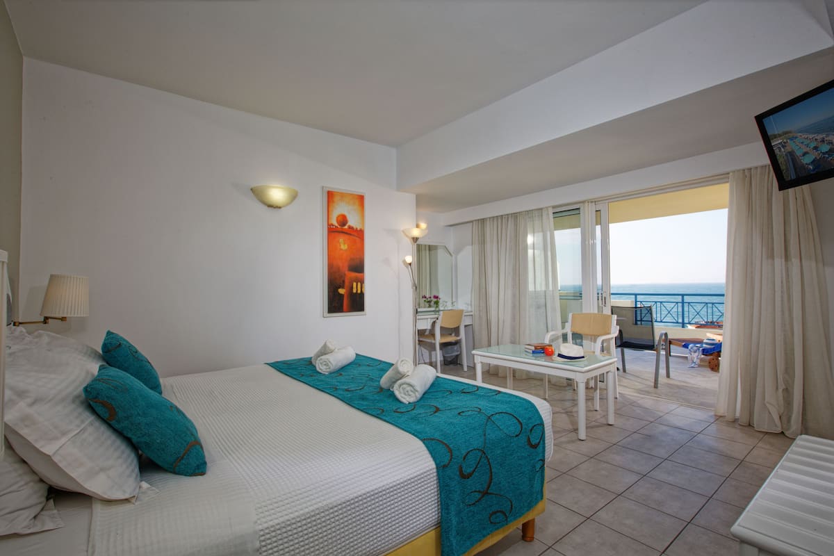 Quarto de hotel com cama, escrivaninha, cadeira e vista para o mar.
