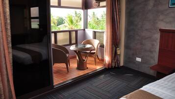 Habitación de hotel con cama, una pequeña mesa con sillas, vistas a palmeras y un balcón con cortinas.