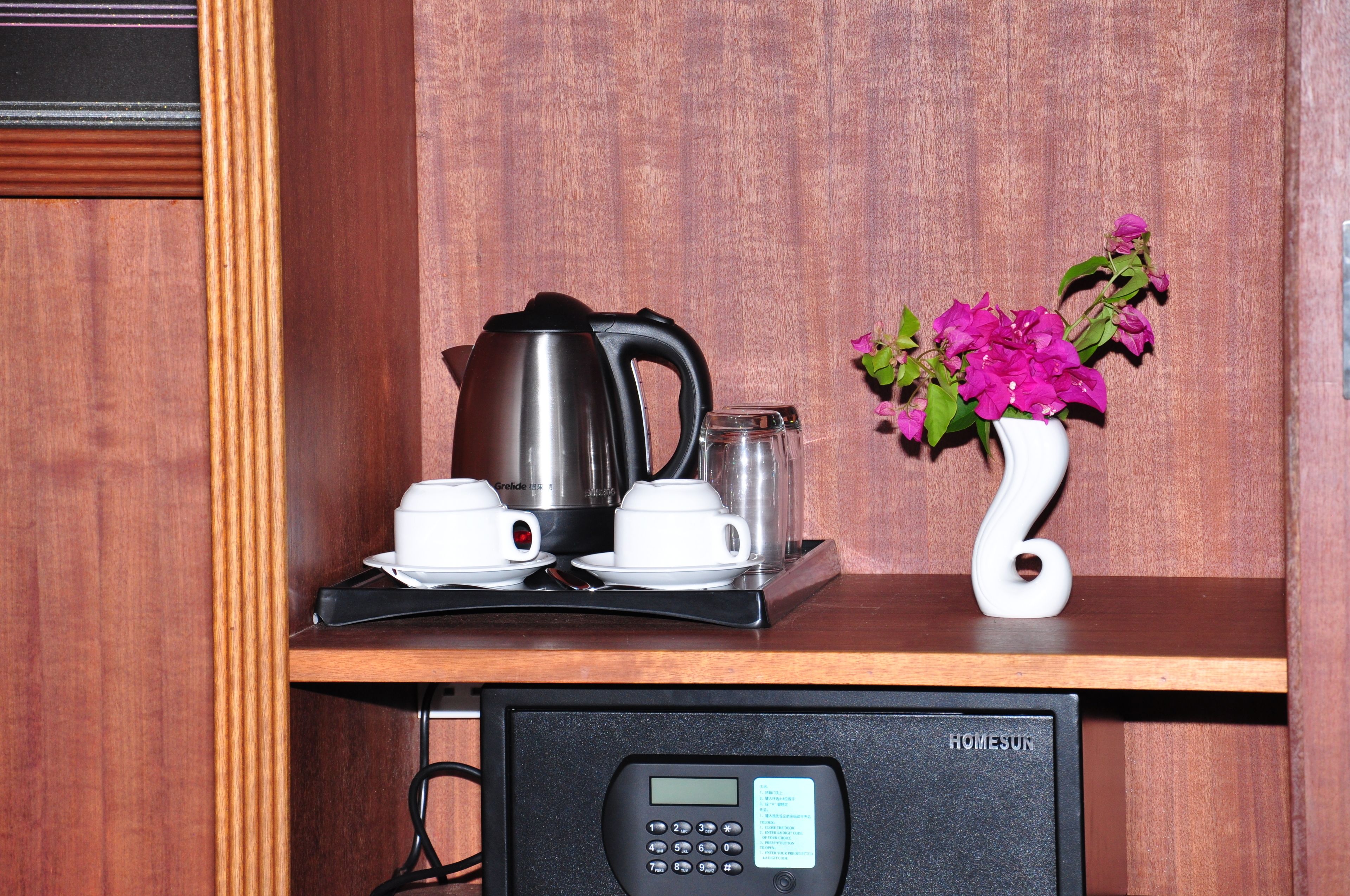 A kitchenette with a coffee maker, cups, a glass jar, and a vase with flowers.