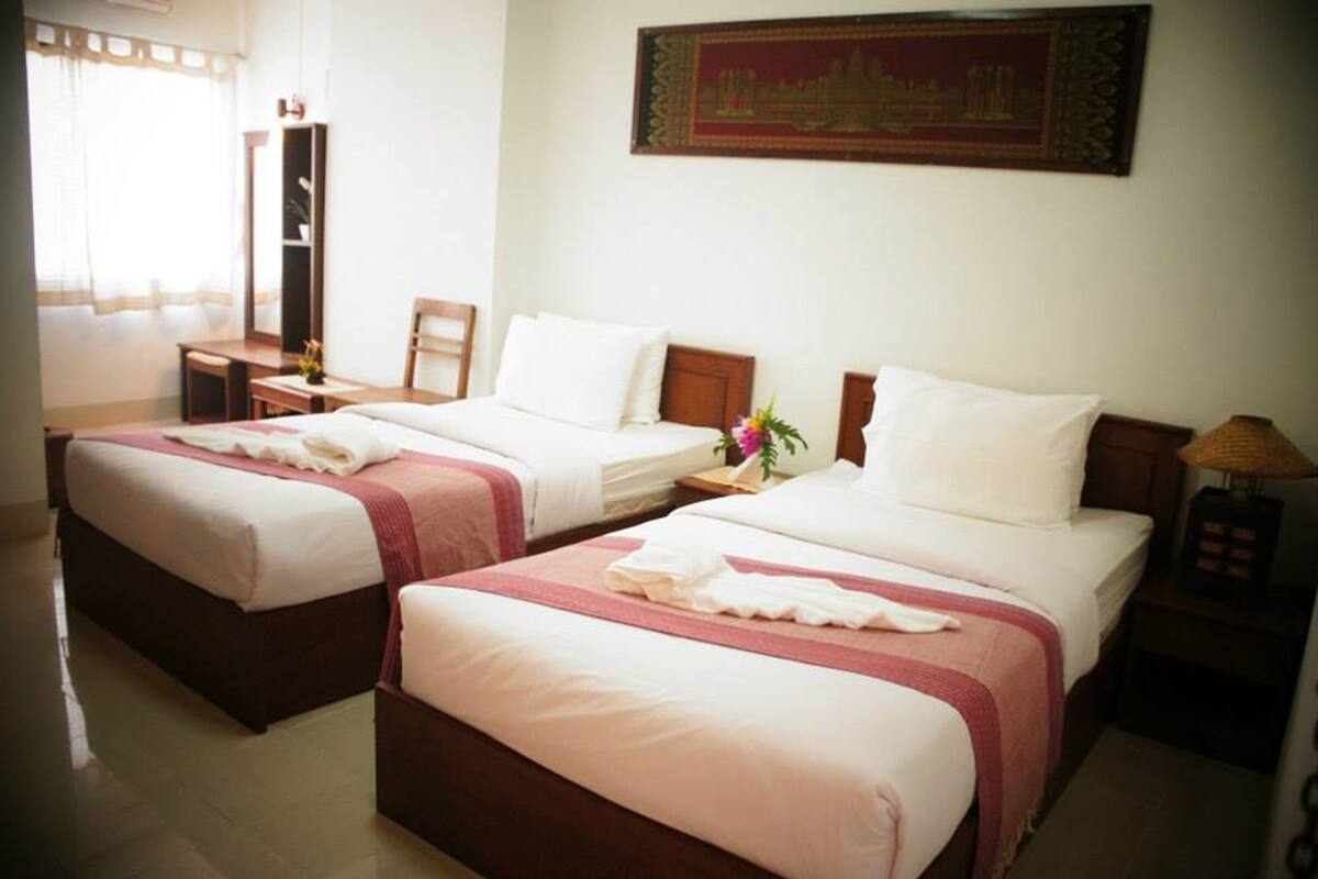 A hotel room with two beds, a desk, a chair, a nightstand with a lamp, and a wall-mounted painting.