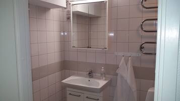 Un baño con azulejos blancos, un lavamanos con un espejo encima y un perchero para toallas.