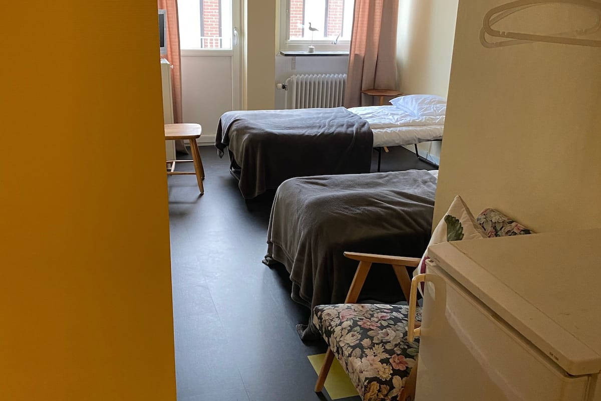 A dormitory room with two beds, a small table, a chair, and a radiator.
