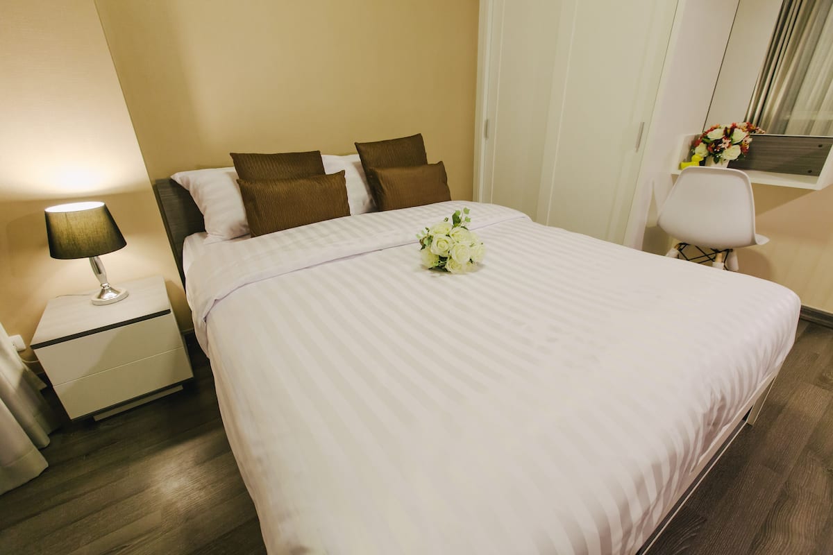 A neatly made bed with a bouquet of flowers, a bedside lamp, and a small table with a chair.