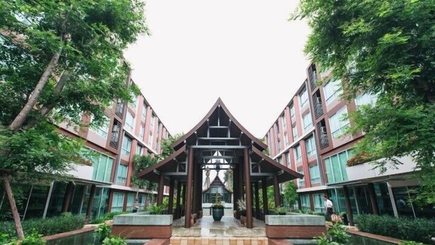 A modern building with a central atrium, surrounded by greenery and water features. - Vienghomnuan Suite Chiang Mai at D.Vieng Condo (Chiang Mai)
