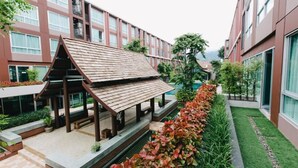 A modern building with a covered outdoor seating area, surrounded by greenery and a well-maintained lawn. - Vienghomnuan Suite Chiang Mai at D.Vieng Condo (Chiang Mai)