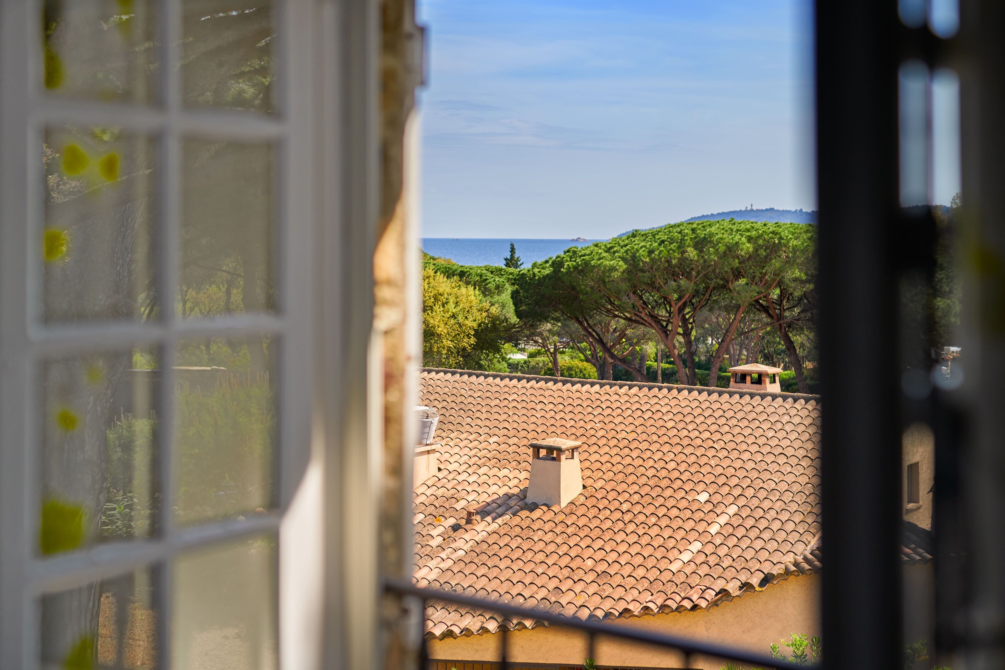 A view through a window of a building with a tiled roof, a chimney, and a distant view of a hill and sea.