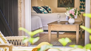 A cozy room with a bed, a wooden table with a vase of flowers, and a wicker chair. - La Ferme d'Augustin (Ramatuelle)